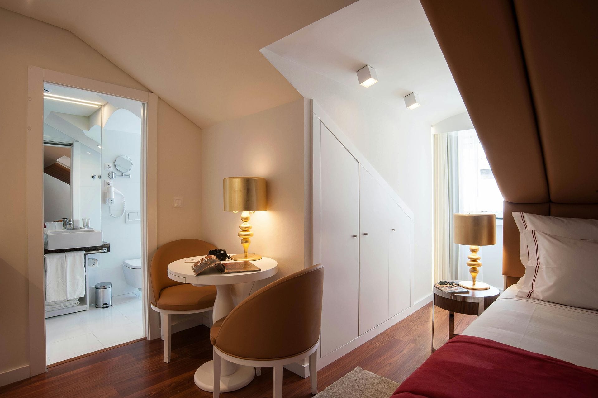 Quarto de hotel boutique em Lisboa com cabeceira em couro caramelo e candeeiros dourados