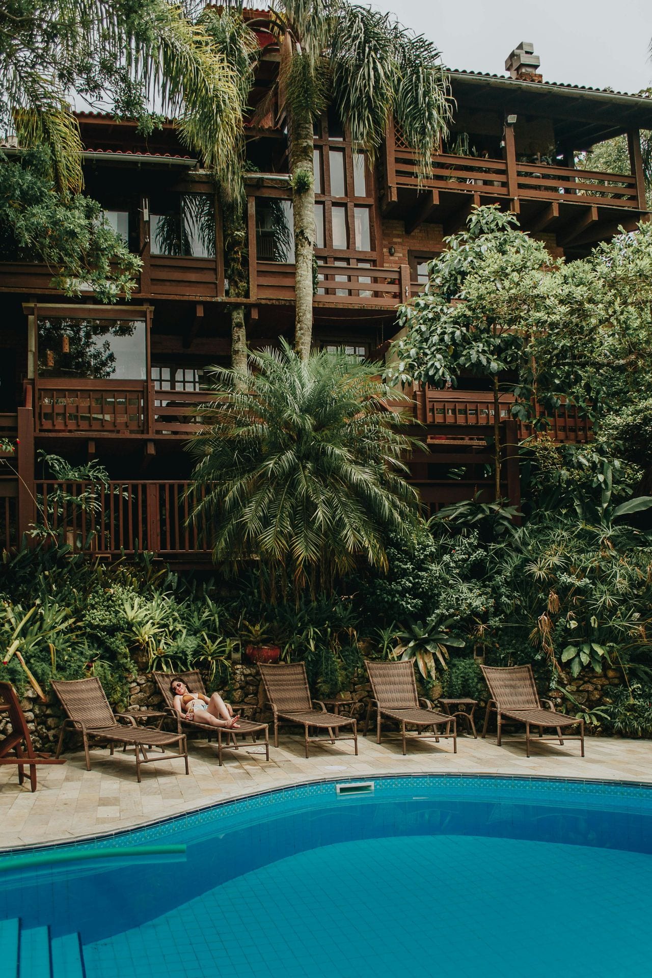 Hotel com fachada em madeira escura, piscina e palmeiras — alojamento boutique