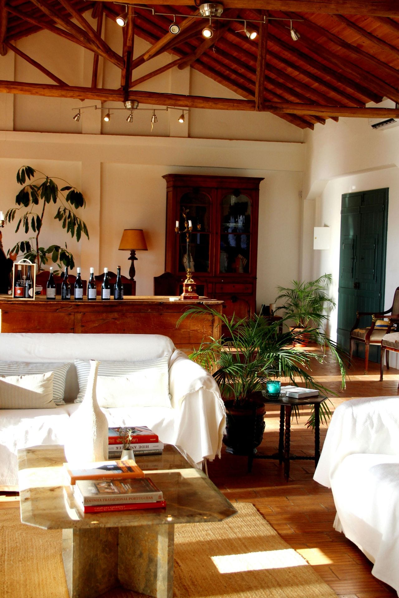 Sala de estar rural portuguesa com sofás brancos, garrafas de vinho e teto em madeira