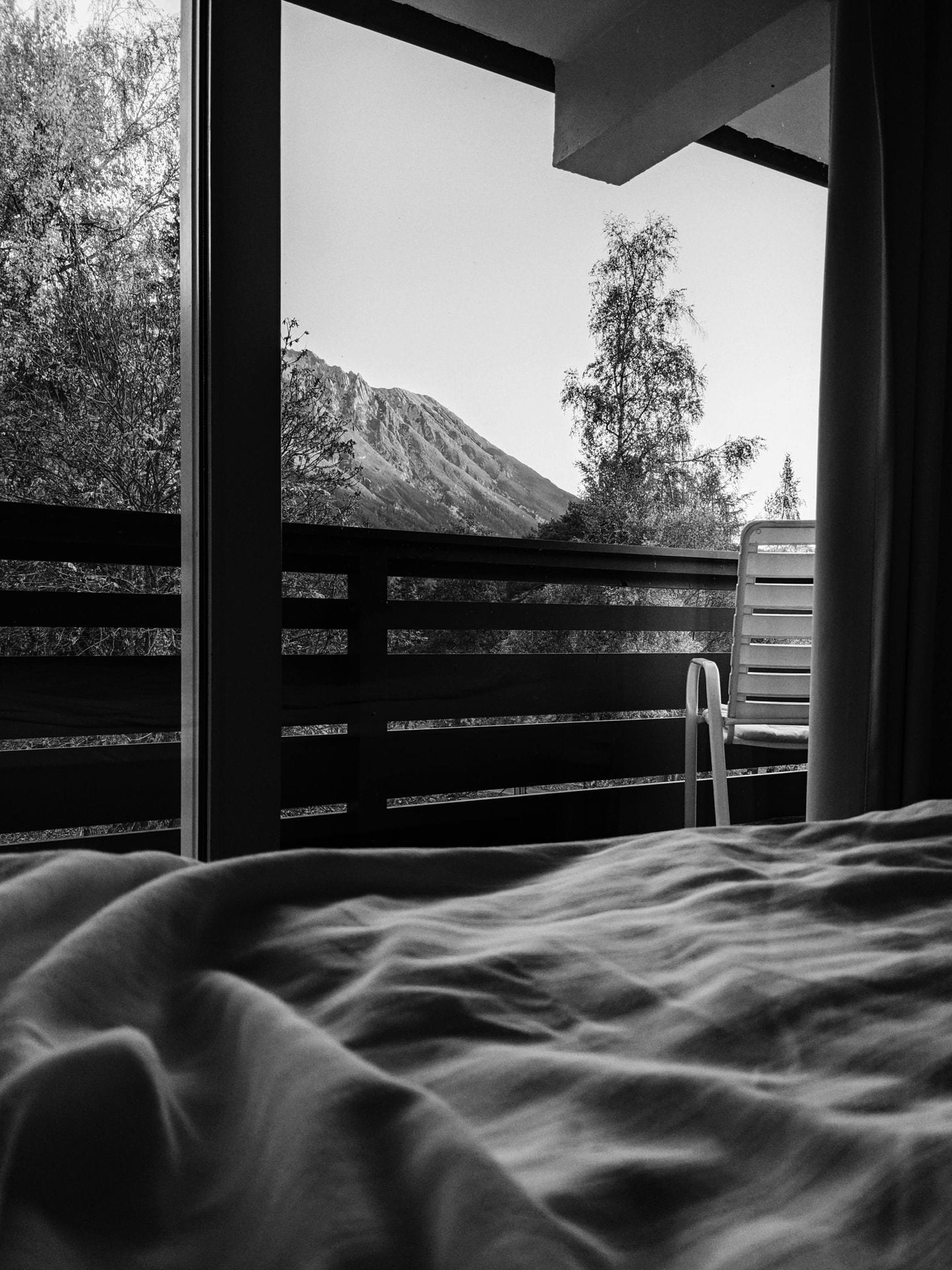 Vista a preto e branco de quarto de hotel com cama desfeita e montanha ao fundo