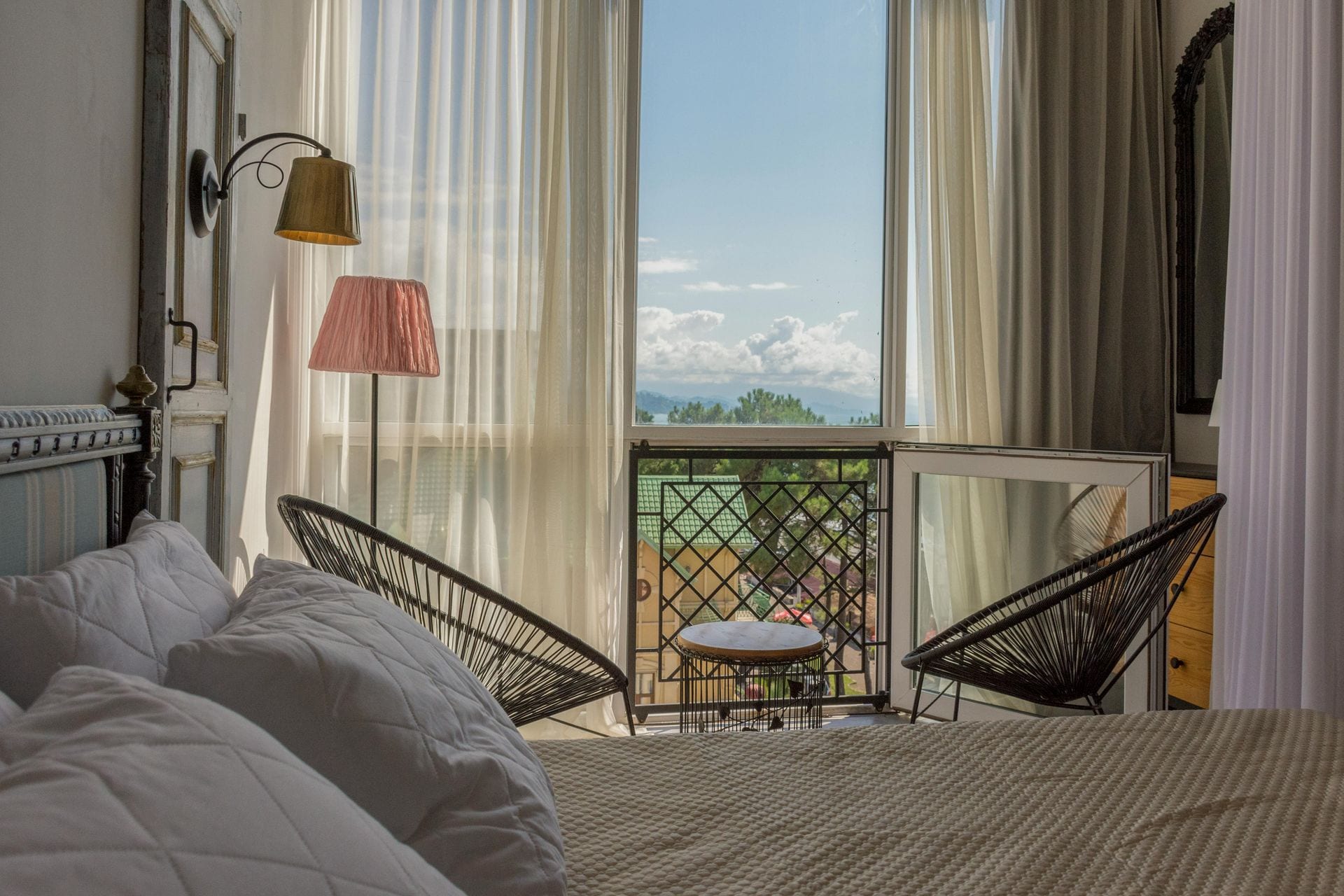 Quarto boutique com cadeiras Acapulco e cortinas leves abertas para varanda com vista de montanha