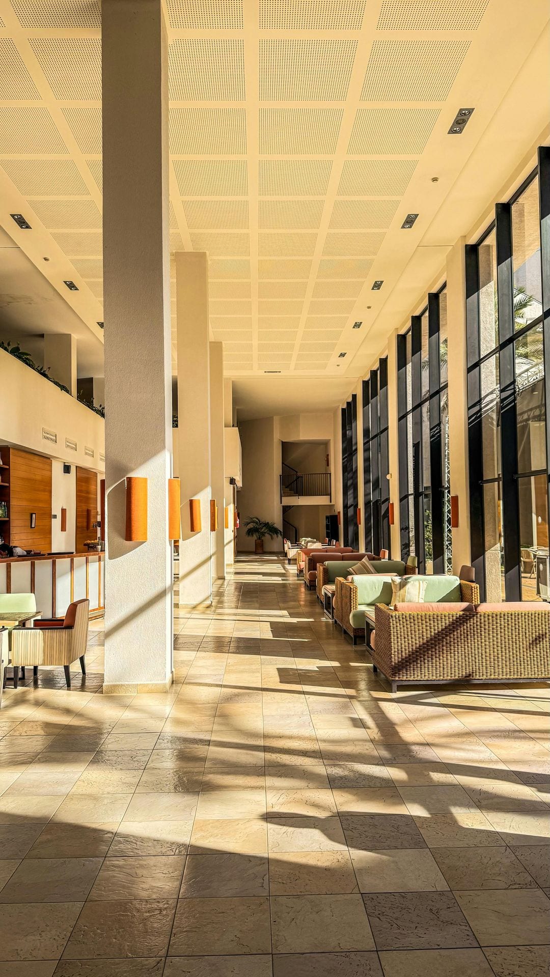 Lobby moderno em travertino com luz natural a entrar pelos vãos altos — observar